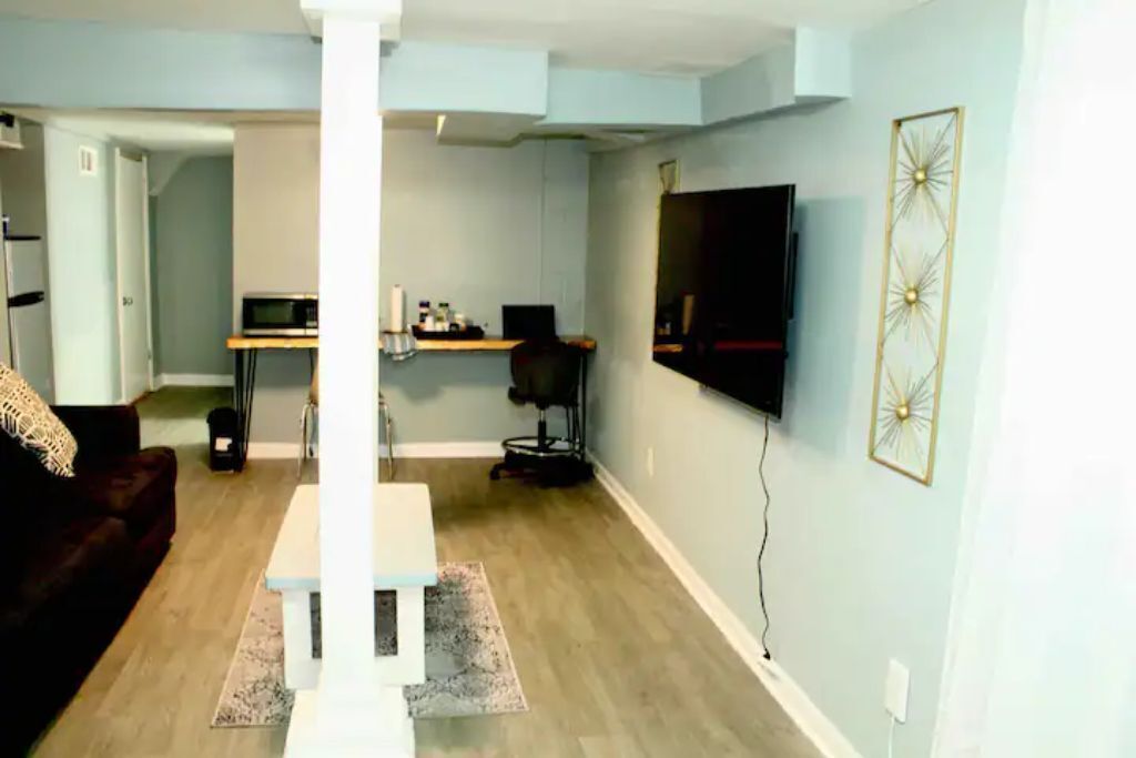 A living room with a dark brown sofa, a white coffee table, and a flat-screen TV mounted on the wall.