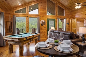 A wooden cabin interior with a pool table, a leather sofa, and a dining table set for four. - NEW!! Mountain Hideaway: Stunning VIEWS, Hot tub, Luxury Touches!  (Gatlinburg)