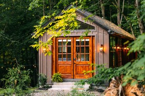 A wooden cabin with a large front door, windows, and exterior lighting.
