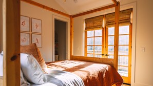 Een slaapkamer met een bed, houten balken, een raam met luxaflex en ingekaderde foto's aan de muur.