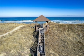A wooden boardwalk leading to a beach gazebo with a clear view of the ocean.