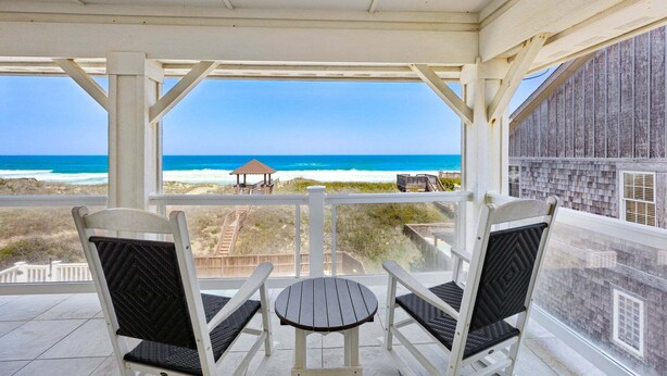 A covered outdoor seating area with two chairs and a table, overlooking the beach. - Happy Sol *9 bedroom*Oceanfront*Elevator*Pool (Nags Head)
