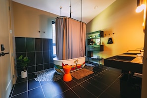 A modern bathroom with a black tiled floor, a shower with a curtain, a small orange stool, a potted plant, and a shelf with toiletries. - Twelve34 House, Penthouse in the Trees, Luxury Hocking Hills, Trails (Laurelville)