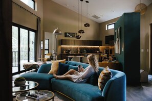 A modern living room with a sofa, a coffee table, and a person using a smartphone. - Twelve34 House+ Penthouse in the Trees + Wall of Glass + Hot Tub (Laurelville)