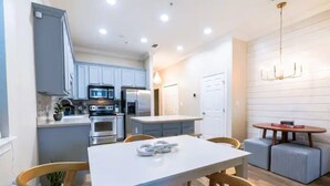 Une cuisine moderne avec des meubles blancs, un coin repas doté d’une table blanche et de chaises en bois, et un lustre.