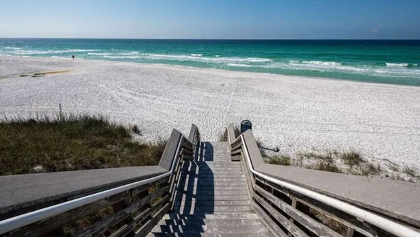 Un escalier en bois mène à une plage d’où l’on a une vue dégagée sur l’océan.