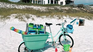 Une scène de plage avec un vélo turquoise, une chaise de plage colorée et un seau vert.