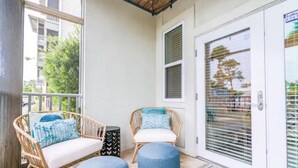 Un balcon avec des meubles en osier, une porte dotée d’une fenêtre et un tapis à motifs.