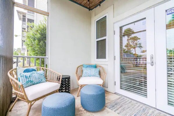 A balcony with wicker furniture, a door with a window, and a patterned rug. - 30A Hideaway. Walk/ride to beach. Bikes included! (Santa Rosa Beach)