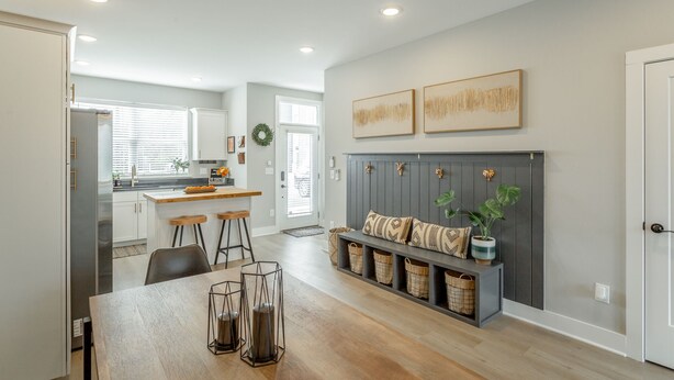 A modern kitchen with a central island, a dining area with a wooden table, and a seating area with a grey headboard and decorative pillows.