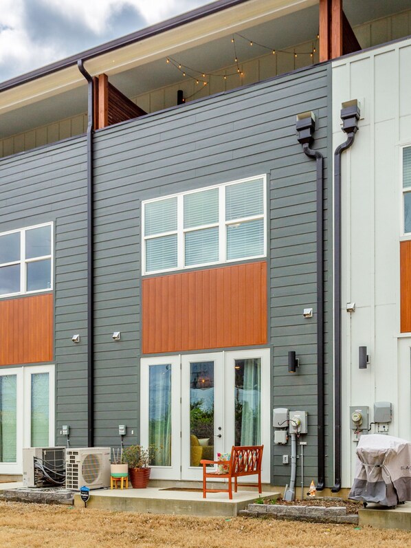 Un bâtiment moderne à deux étages, doté de grandes fenêtres, d’une terrasse en bois et de mobilier d’extérieur.