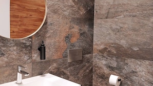Ein Badezimmer mit modernem Design, ausgestattet mit einem runden Spiegel, einem weißen Waschbecken und einem Toilettenpapierhalter an der Wand.