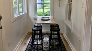 A narrow hallway with a wooden table and two black barstools, a patterned rug, and a window with a view of greenery and a house. - Parkman Pad: hot tub, wood stove by Montague breweries (Montague)