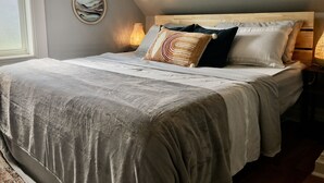 A bedroom with a large bed, a wooden headboard, and a bedside lamp. - Parkman Pad: hot tub, wood stove by Montague breweries (Montague)