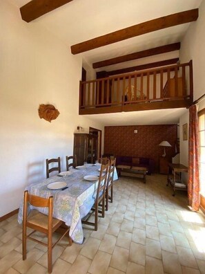 A dining area with a table set for four, wooden chairs, a bench, and a small table with a lamp.