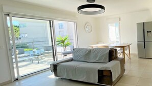 A modern living room with a sofa, a dining table, and a kitchen area. - Superb 3P in a quiet location Swimming pool Terrace Barbecue Pétanque aircon (ANTIBES)