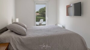 A bedroom with a large bed, a TV mounted on the wall, and a view of the outdoors through a door. - Superb 3P in a quiet location Swimming pool Terrace Barbecue Pétanque aircon (ANTIBES)