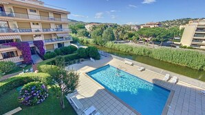 A swimming pool with a view of a river, surrounded by greenery and a building with balconies. - New T2 apartment for 4 people in residence with swimming pool (SAINTE MAXIME)