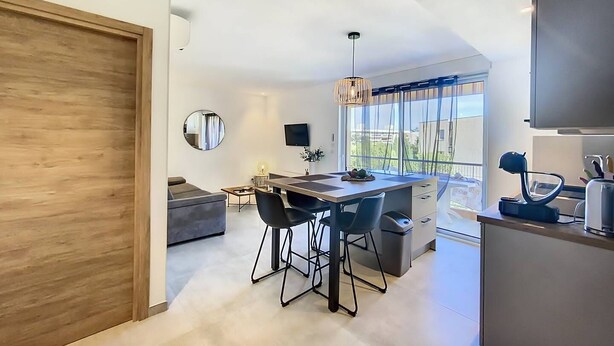 A modern kitchen with a dining area, a large window, and a TV mounted on the wall. - New T2 apartment for 4 people in residence with swimming pool (SAINTE MAXIME)