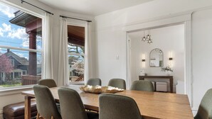 Ein Essbereich mit einem Holztisch, sechs Stühlen, einer großen Dekorationsschale und Blick auf ein Haus durch ein Fenster.