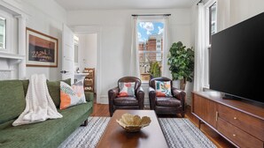 Ein Wohnzimmer mit einem grünen Sofa, zwei Ledersesseln, einem Couchtisch aus Holz und einem großen Flachbildfernseher.