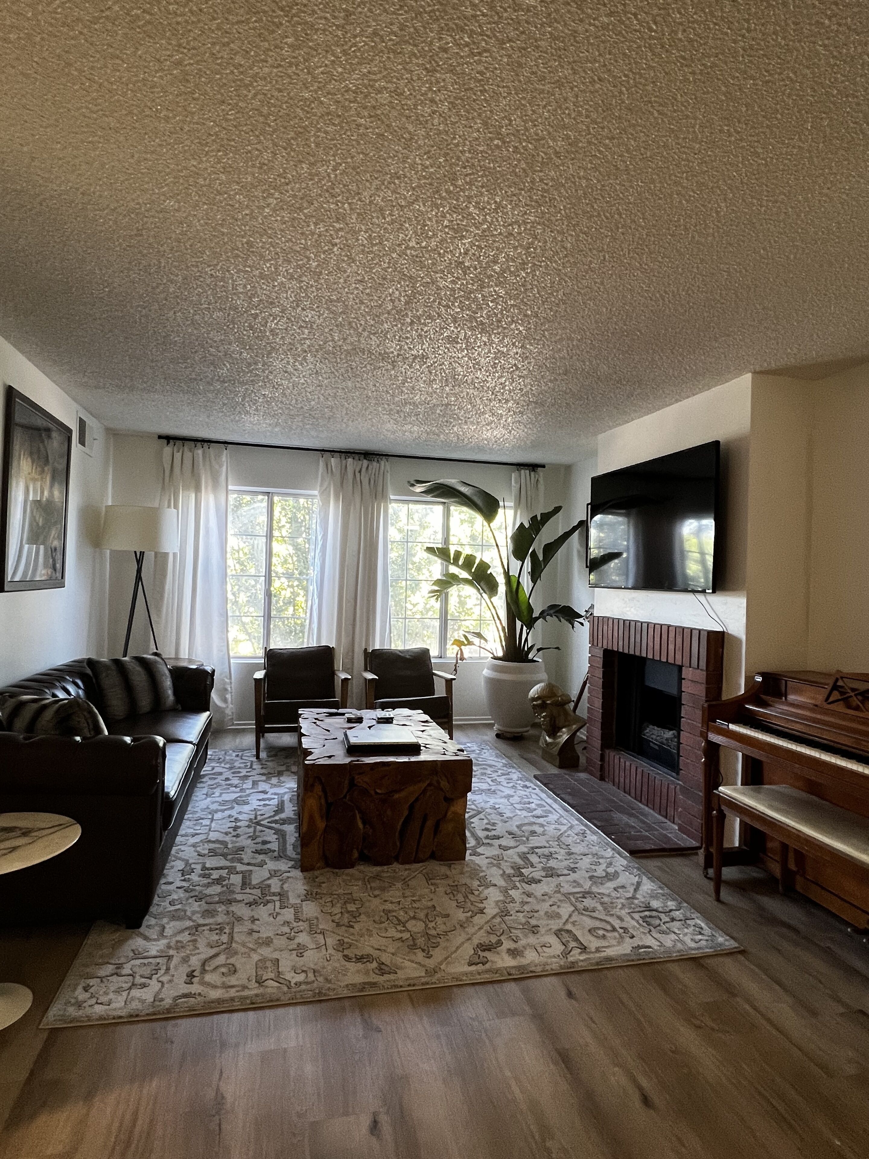 Un salon comprenant un canapé, des fauteuils, une table basse, une cheminée, un téléviseur et un piano.