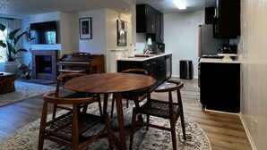 Een moderne keuken met zwarte kastjes, een eethoek met een ronde houten tafel en stoelen, en een hanglamp.