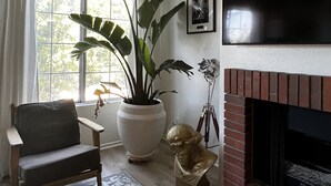 Een woonkamer met een open haard, een grote potplant, een beeld en een tv aan de muur.