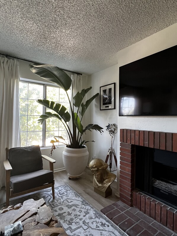 A living room with a fireplace, a large potted plant, a statue, and a mounted television.