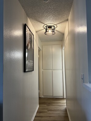 Leading to a space, this hallway features a framed picture and a ceiling light fixture.