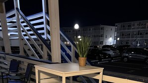Et hvidt metalbord og to stole på et mønstret tæppe, med en trappe og gelænder i baggrunden.
