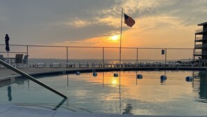 En swimmingpool med en træterrasse, liggestole og udsigt til solnedgangen over havet.