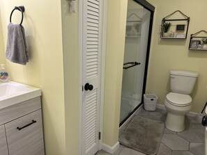 A bathroom with a toilet, a glass shower enclosure, a sink with soap dispenser, and a towel hanging on the wall. - Beautiful bayside first level condo!  Quick walk to the beach. (Ocean City)