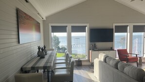 Ett rymligt vardagsrum med ett matbord, sittplatser och stora fönster som erbjuder utsikt över havet och en brygga.