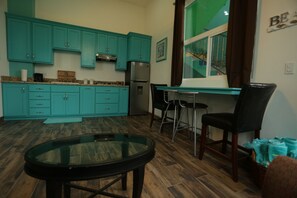 A kitchen with teal cabinets, a refrigerator, a dining table with chairs, and a window with curtains. - Trojan House Blue Suite (Ensenada)