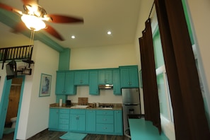 A kitchen with teal cabinets, a stainless steel refrigerator, and a ceiling fan. - Trojan House Blue Suite (Ensenada)