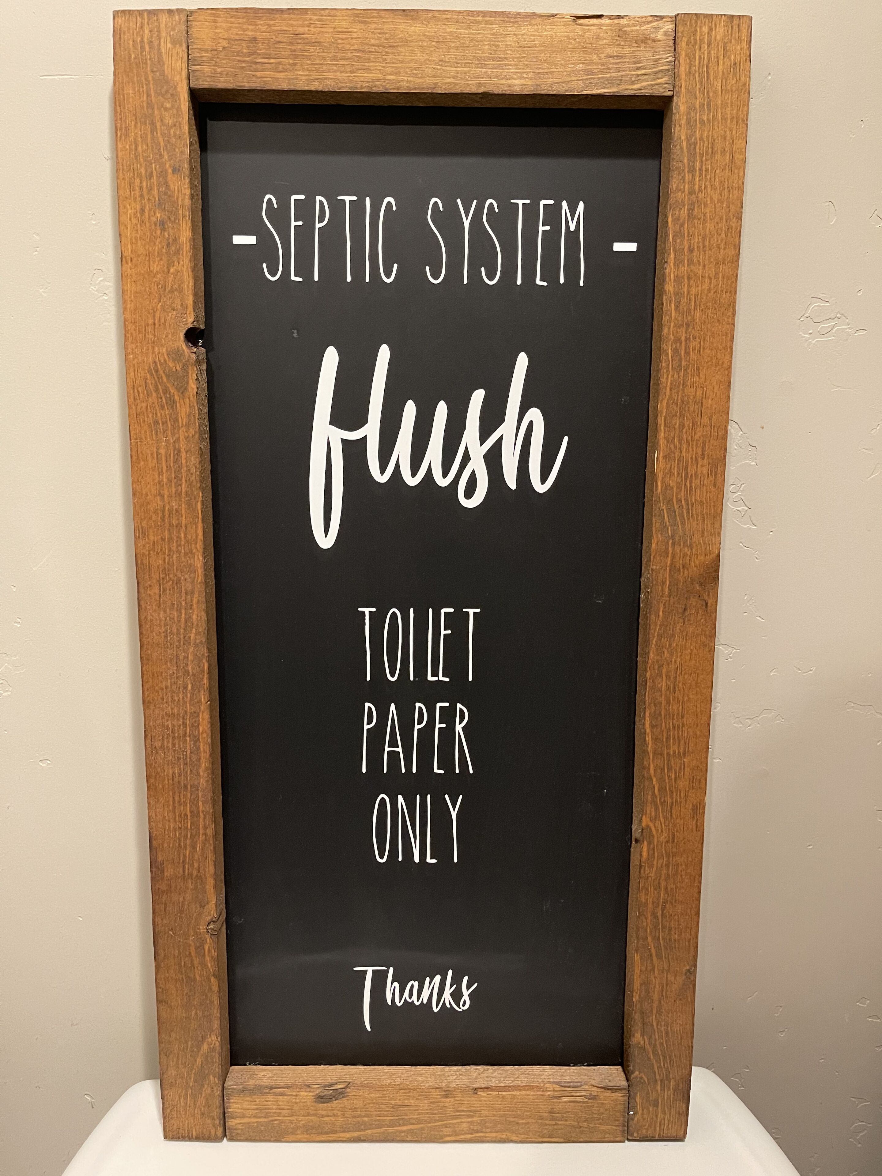 Une pancarte encadrée portant le texte « SYSTÈME D’ASSIAINISSEMENT – NE JETER QUE DU PAPIER TOILETTES » et le mot « Merci » en bas.