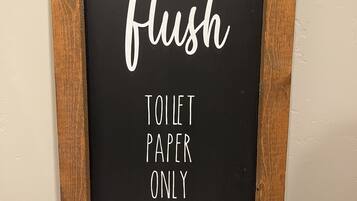 Une pancarte encadrée portant le texte « SYSTÈME D’ASSIAINISSEMENT – NE JETER QUE DU PAPIER TOILETTES » et le mot « Merci » en bas.
