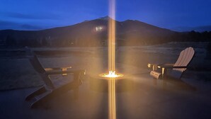 Un foyer avec deux fauteuils Adirondack placés en face, le tout sur fond de montagnes au crépuscule.