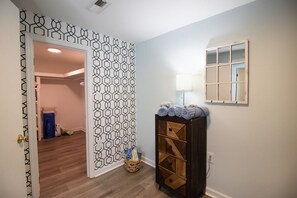 A hallway with a geometric-patterned wall, a wooden cabinet with towels, a lamp, and a window with a white frame.