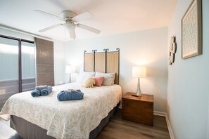 Un dormitorio con cama, ventilador de techo, mesita de noche, lámpara y ventana con persianas.