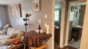 A cozy living room with a sofa, a coffee table, and a small wooden stool. There is a decorative flower on the wall and a lamp.