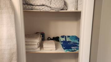 A storage area with shelves holding folded towels, a patterned blanket, and a clear plastic basket.