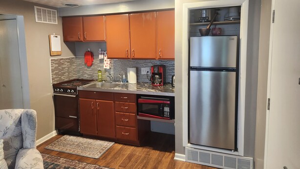 A compact kitchen with wooden cabinets, a stainless steel refrigerator, a microwave, and a gas stove.