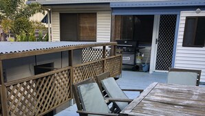 Une terrasse dotée d’une table et de chaises en bois, d’un barbecue et d’un espace patio couvert.