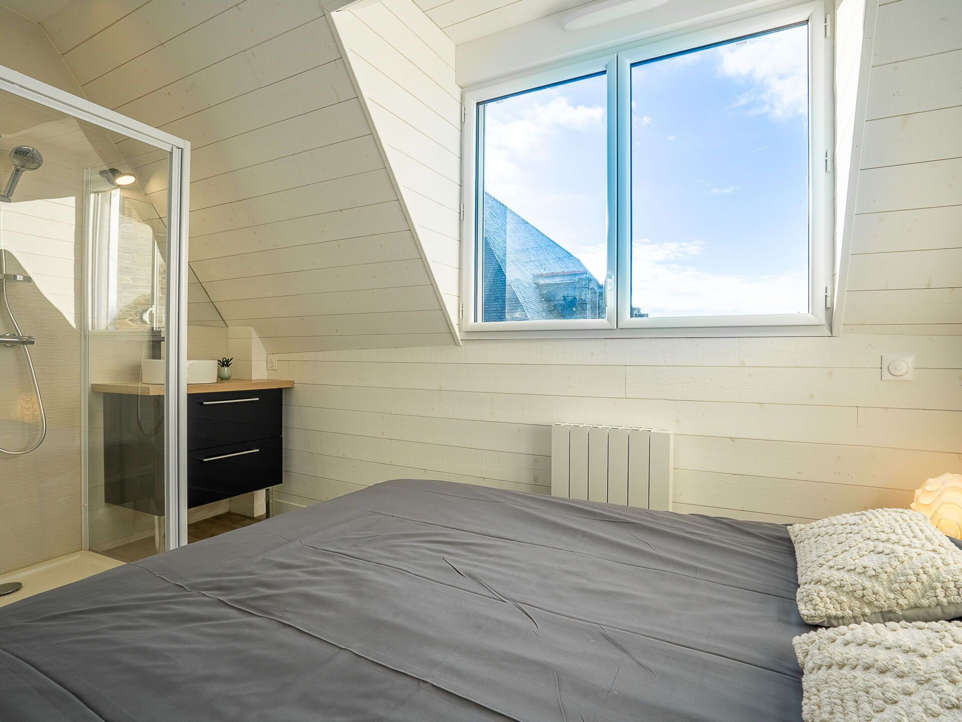 A bedroom with a skylight, a shower, and a view of a building.