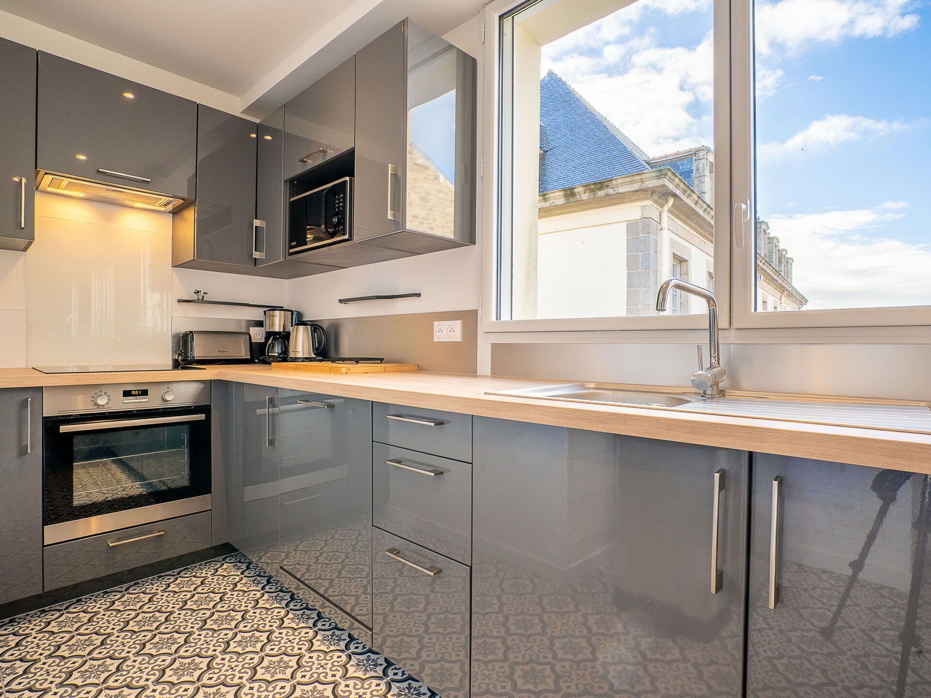 Una cocina moderna con un ventanal grande, electrodomésticos de acero inoxidable y baldosas de suelo con diseño.