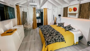 A bedroom with a bed, a desk, a hanging chair, and a TV. - Mango Cottage Orient Bay, Charming and Authentic (Collectivité de Saint-Martin)