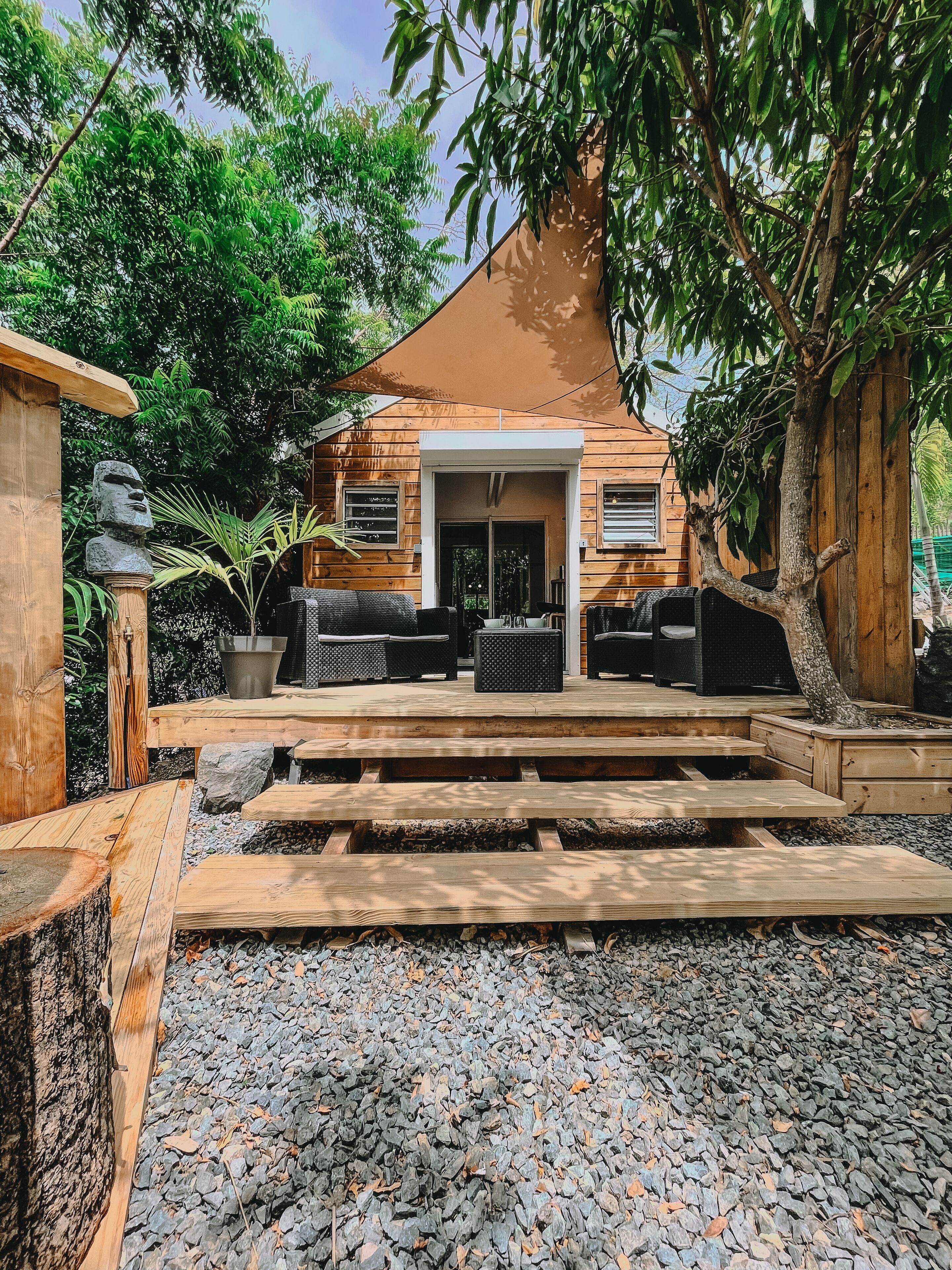 A wooden house with a covered patio, outdoor seating, and a stone statue.