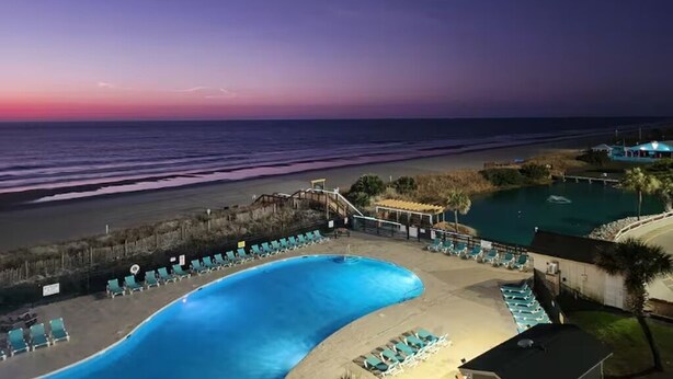 A pool area with lounge chairs, a beach, and a sunset view. - Retreat by the Sea (Myrtle Beach)